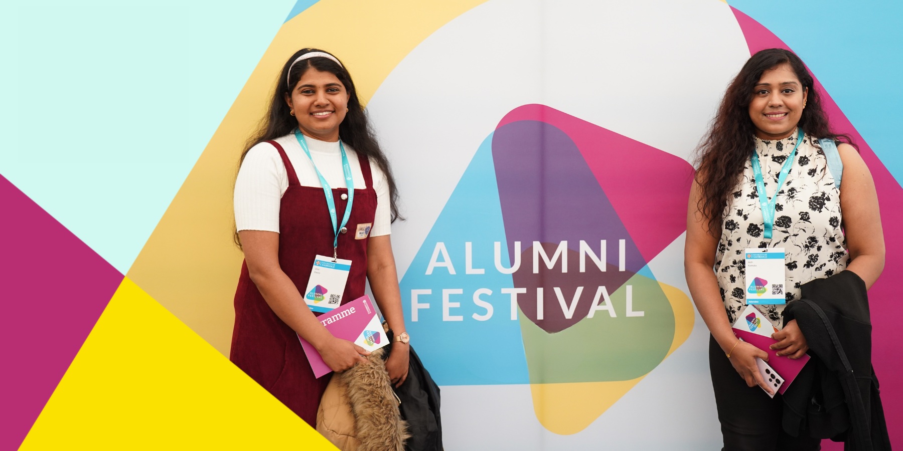 Two people standing in front of the Alumni Festival banner