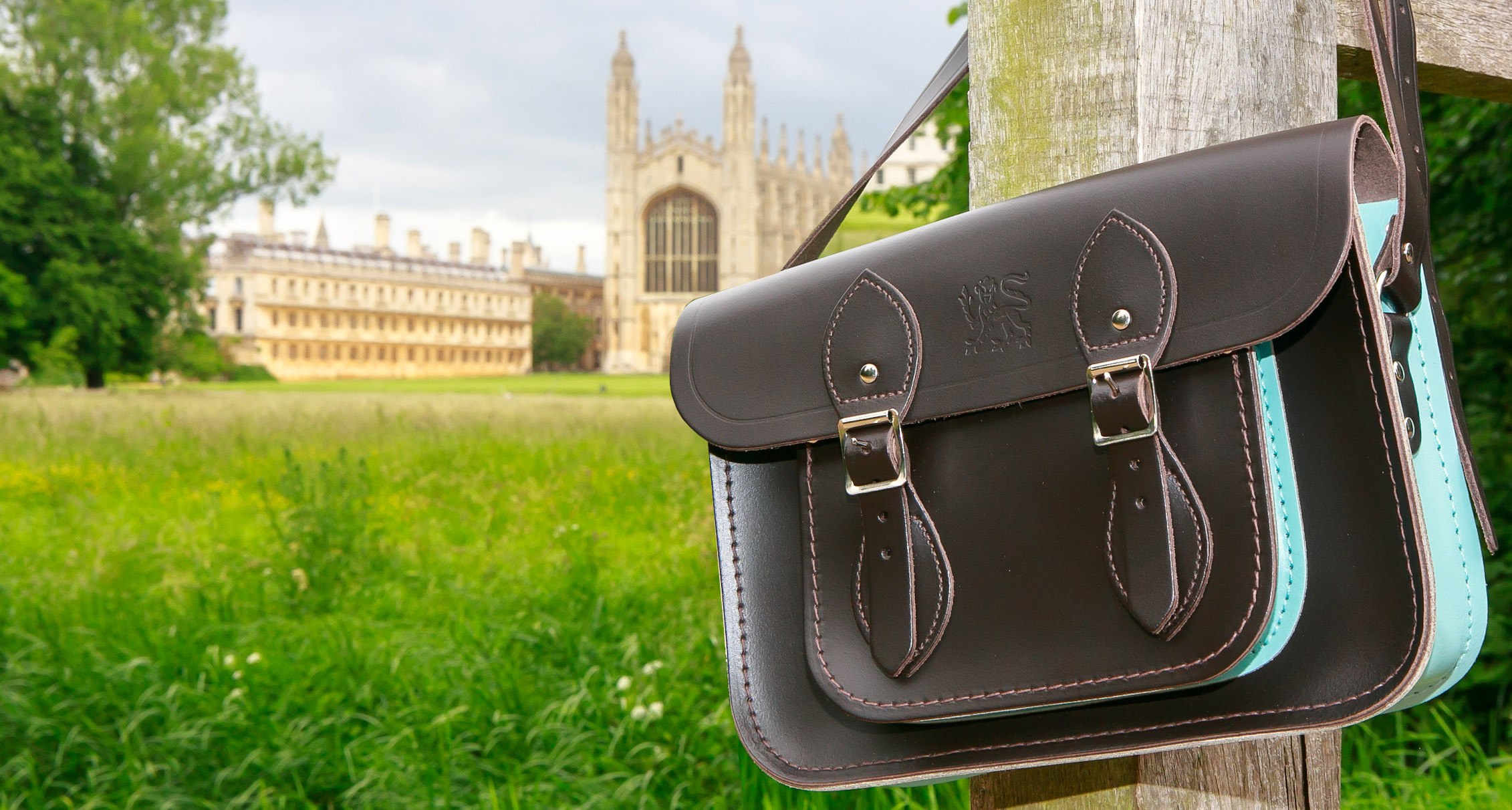 Brown leather satchel hanging on a woodne post with King's College across the green in the background