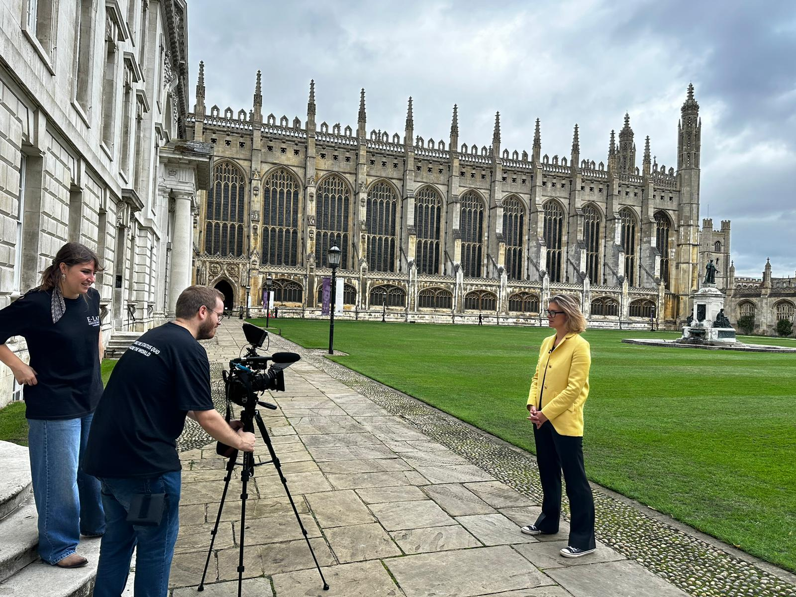 Ali Draycott stood in front of Kings College chapel whilst 2 people operate a camera to interview her