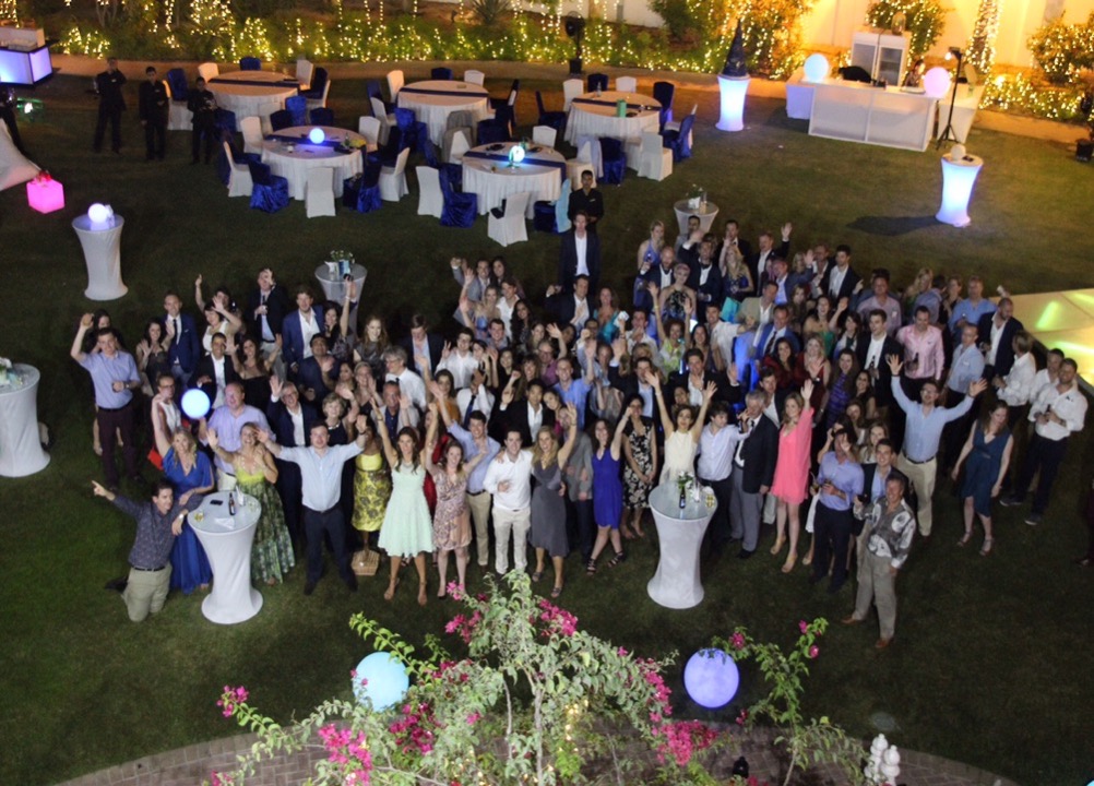 Large group of people smiling up at a formal event surrounded by cocktail tables