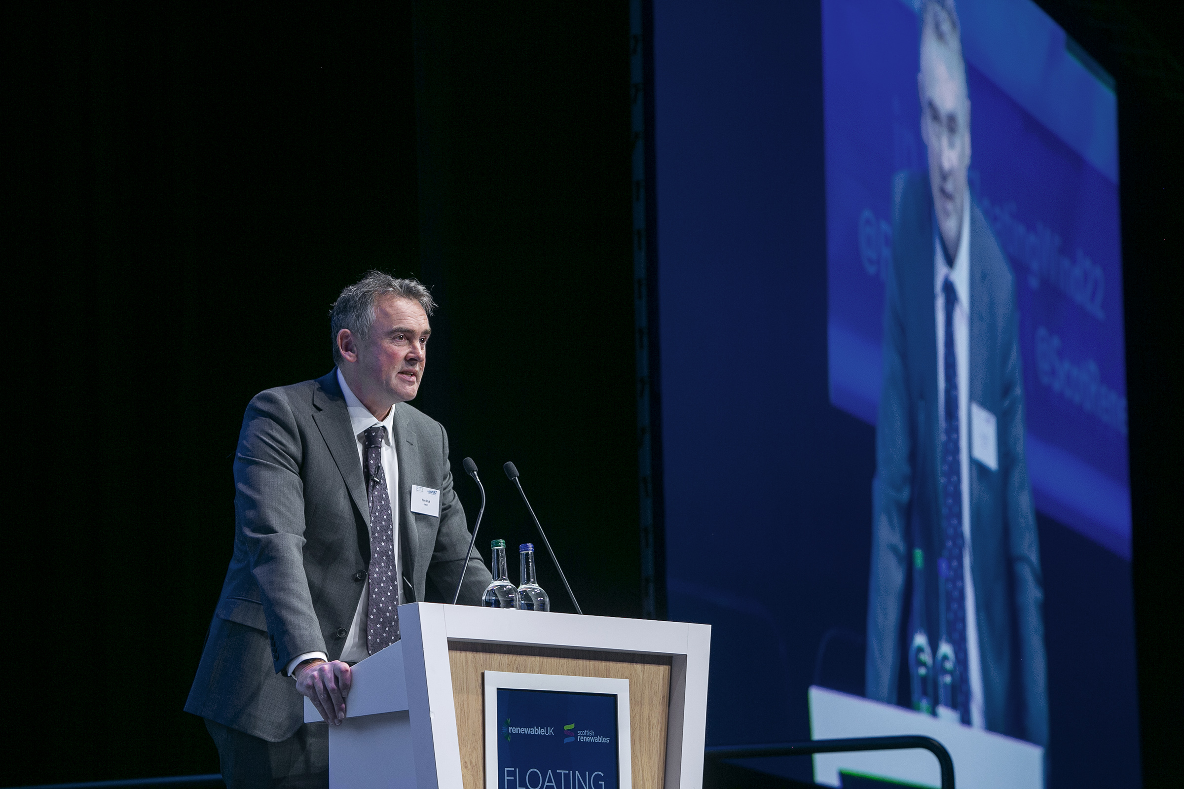 Photograph of Tom Pick MBE standing at a lectern delivering a speech at a conference