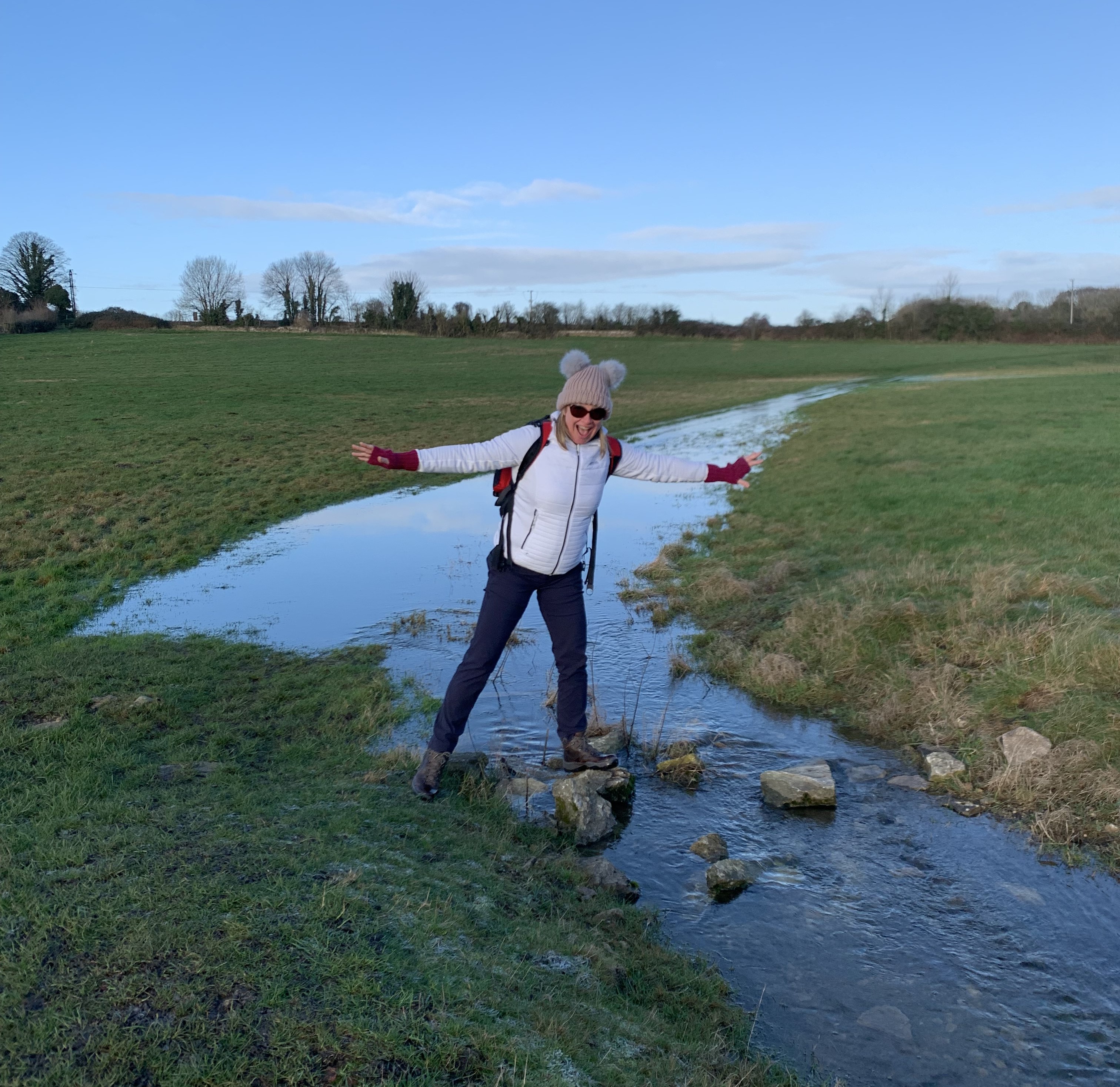 Claire stands in outdoor gear on a stepping stone at the source of Thames.