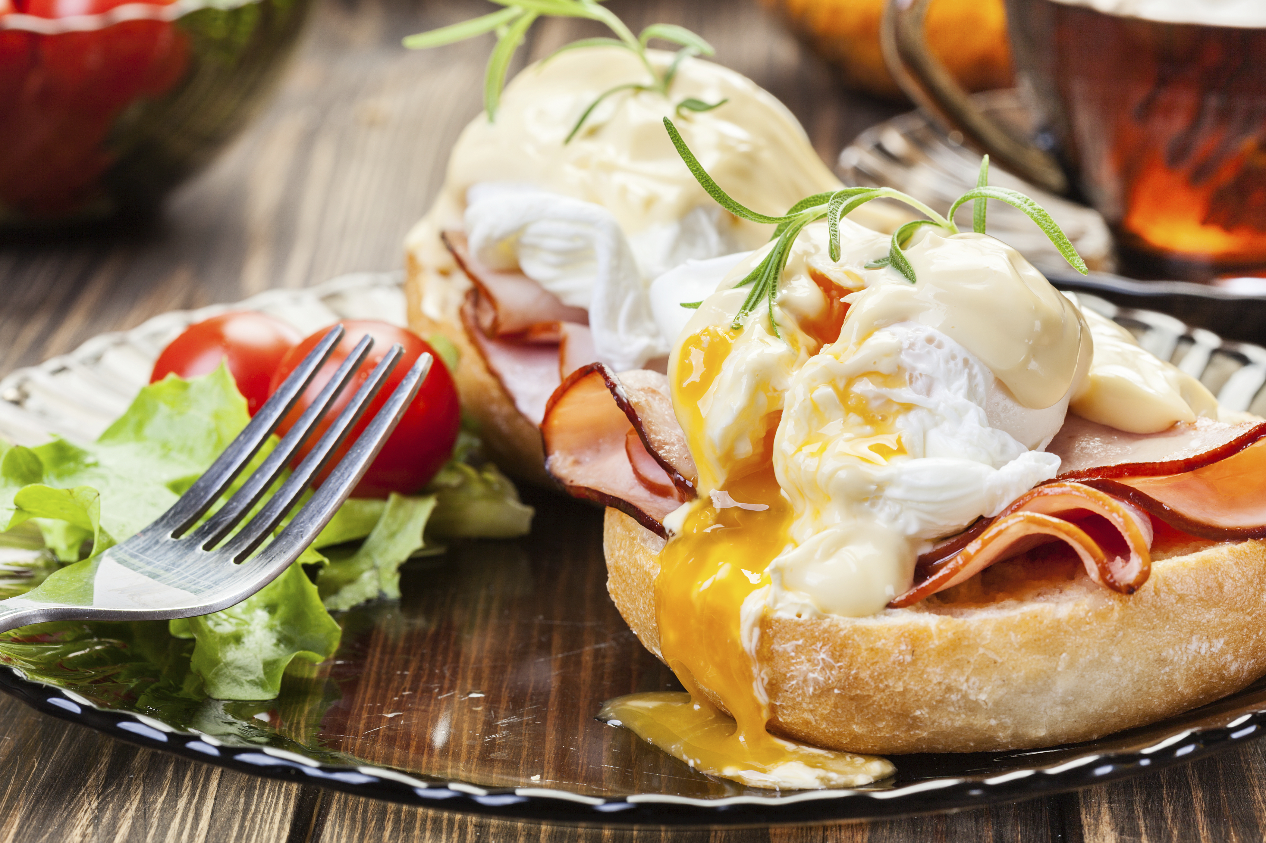 Eggs benedict on a muffin with a fork and ham