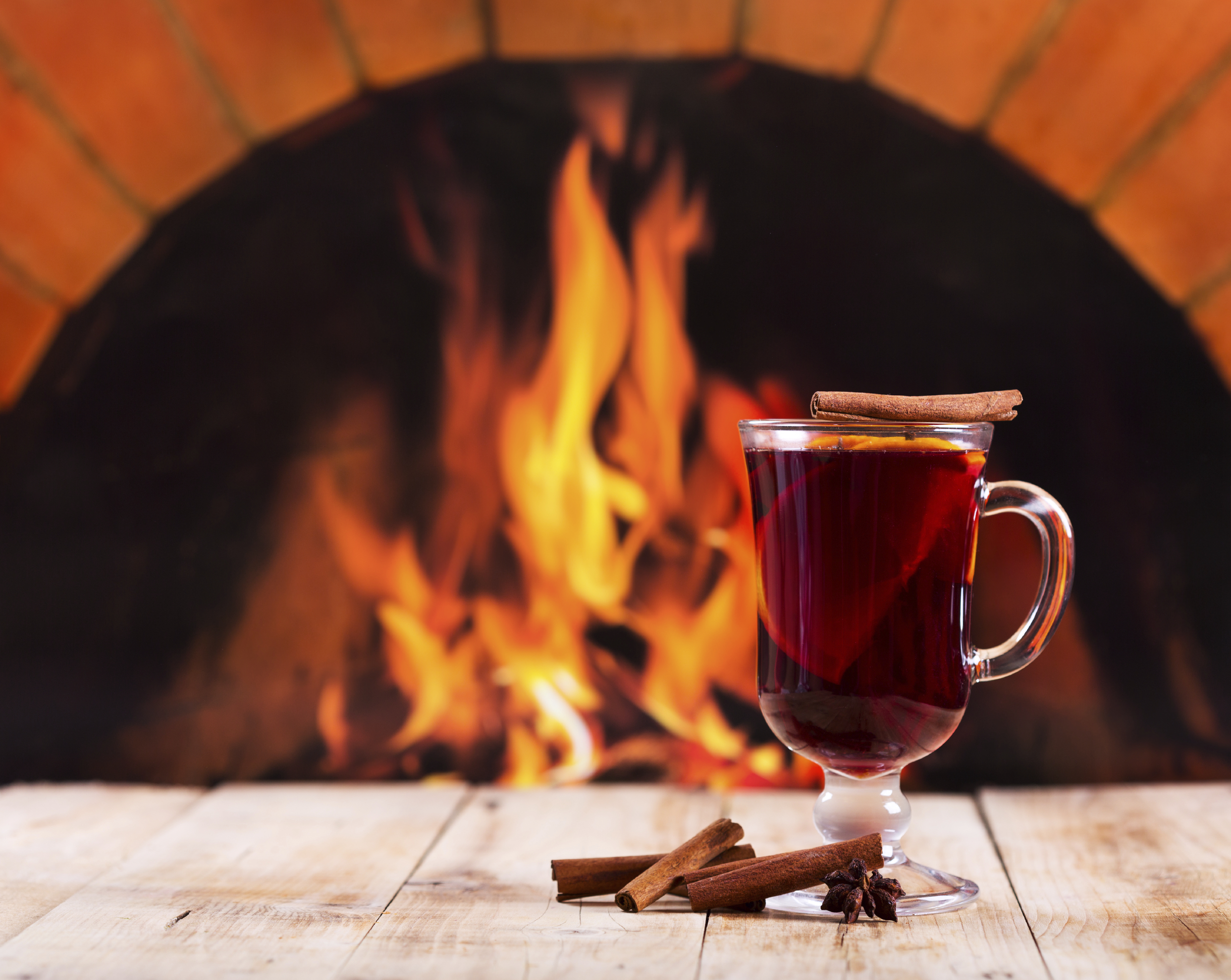 A glass of mulled wine in front of a roaring fire