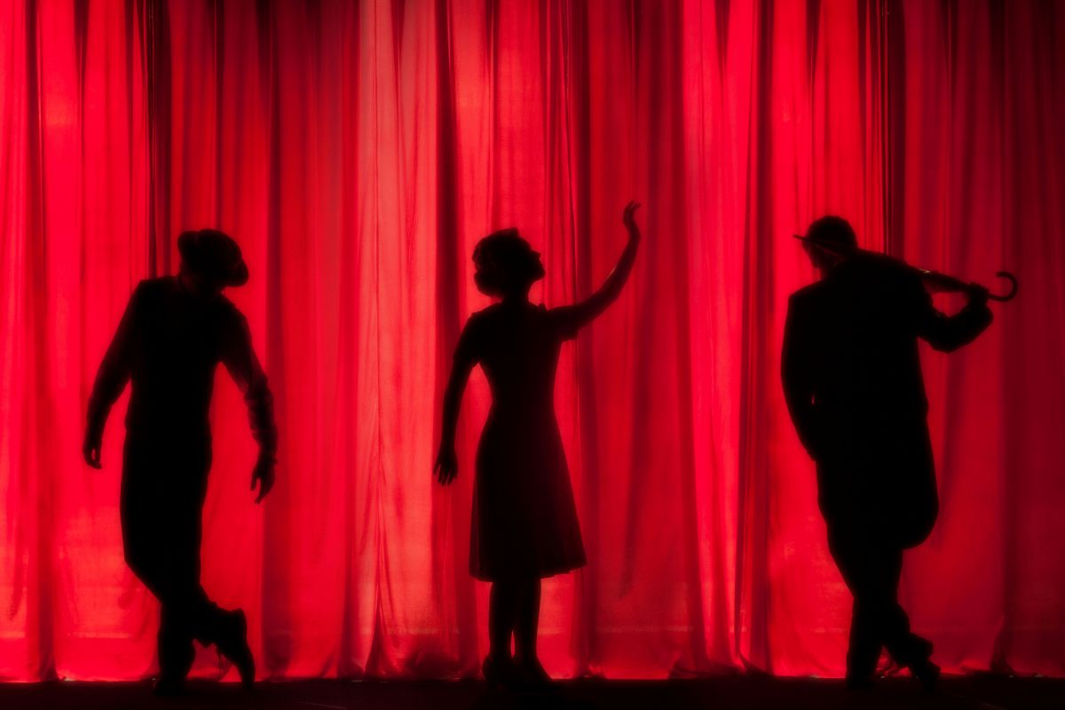 Three actors on a stage in front of a red curtain