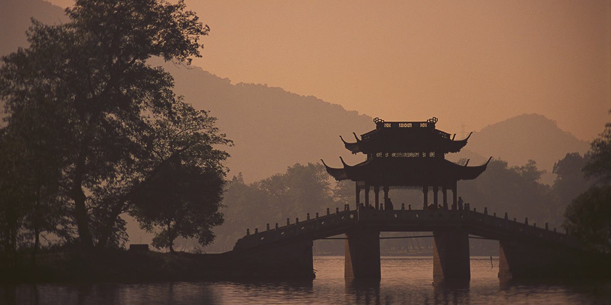 Chinese garden bridge over a lake in silhouette in orange humes