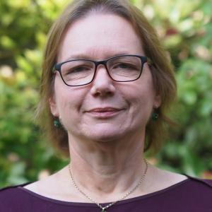 Headshot of Alison, wearing glasses, necklace and burgundy top with green background