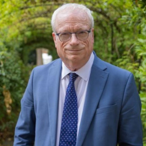 photograph of The Rt Hon Lord Smith of Finsbury wearing a blue suit and tie against a backdrop of green trees