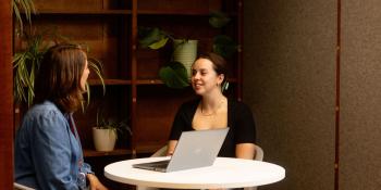 Two women talking around a small tablet with a laptop on it