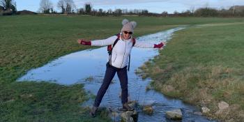Claire stands in outdoor gear on a stepping stone at the source of Thames.