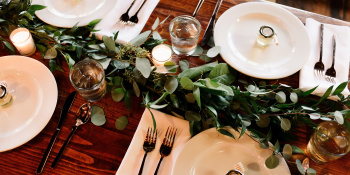 Overhead view of a dinnertable that has been set for a meal, there's candles and a selection of forks and green leaves