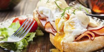 Eggs benedict on a muffin with a fork and ham