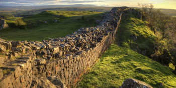 Hadrian's Wall in focus surrounded by green fields.