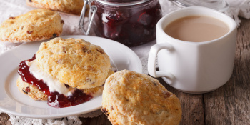 Scones filled with jam and cream sit on a plate alongside a cup of tea and a jar of jam.