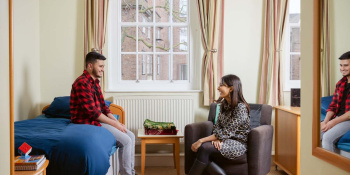 Dharshini David sits on chair chatting to Jiyaad Ali who sits on bed.