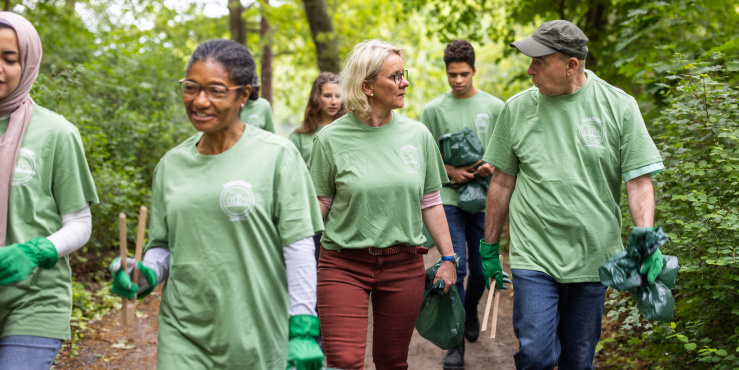 Getty image library photograph showing a group of volunteers walking through a wooded location in green tops and carrying tools