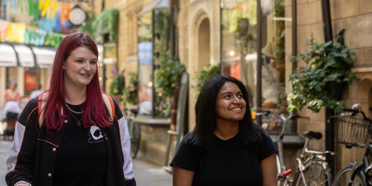 Two Cambridge students walking through Rose Crescent, central Cambridge, looking at shop windows while talking.