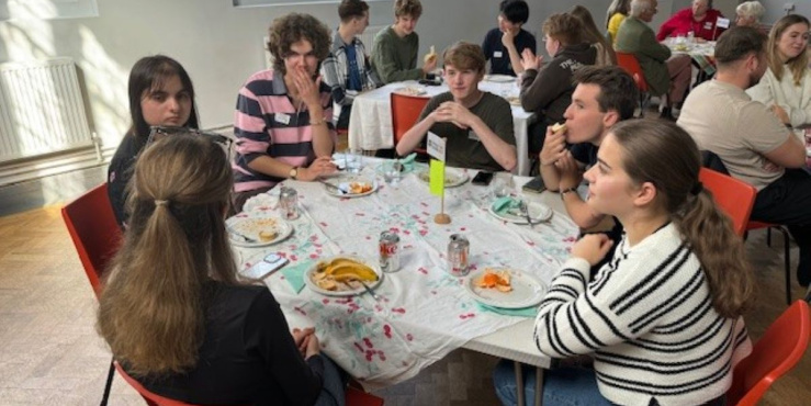 A group of freshers at a table talking and eating snacks