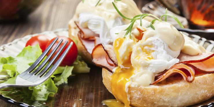 Eggs benedict on a muffin with a fork and ham