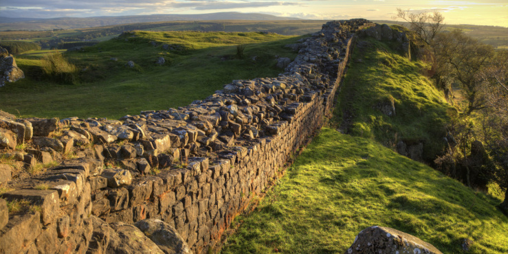 Hadrian's Wall in focus surrounded by green fields.