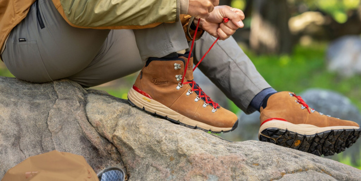 Hiker tying up their hiking boots whilst sat on a rock.