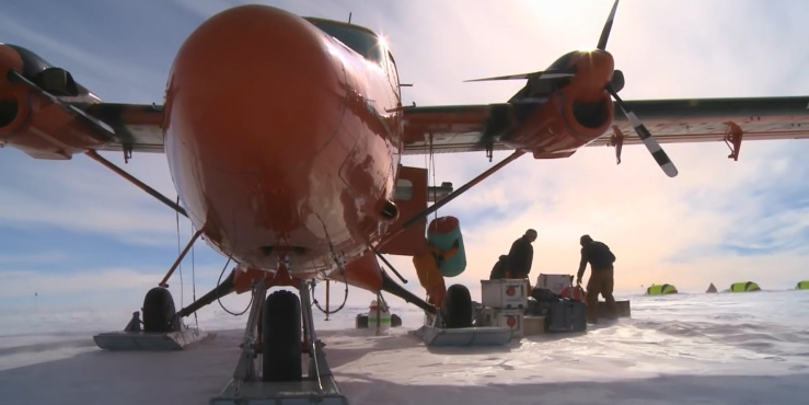 A plane sits in a snowy landscape while researchers unload cargo