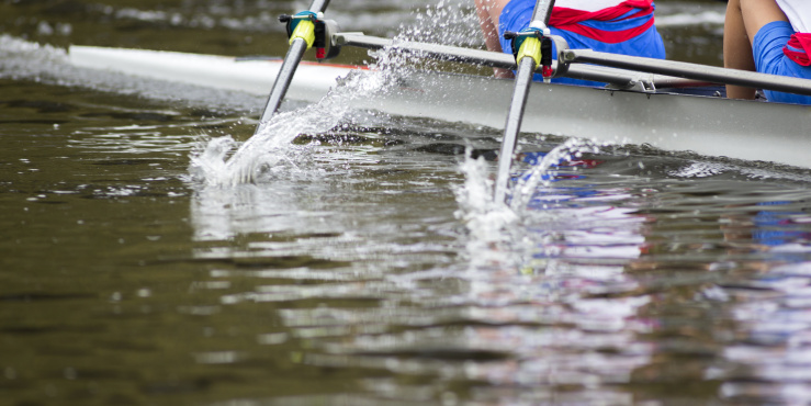 Rowers on a river, oars splashing into the water