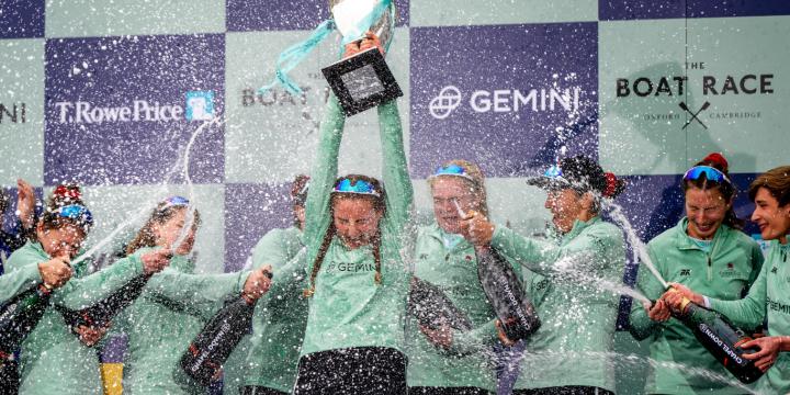 The 2023 women's crew celebrate victory, holding the trophy high and spraying champagne.