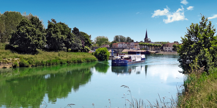 Blue barge sailing down a river, in the background a church spire