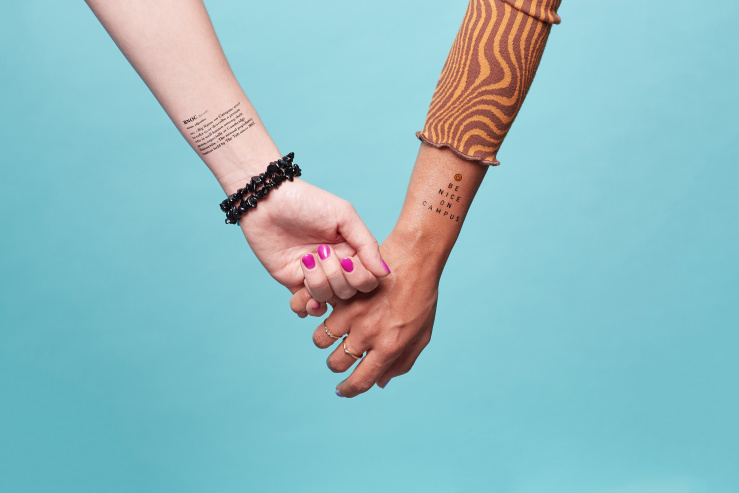 Two people hold hands. Both have BNOC temporary tattoos on their arms.