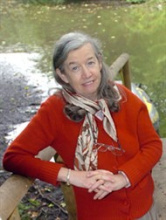 Rowena archer wearing a red cardigan, lending on a wooden post