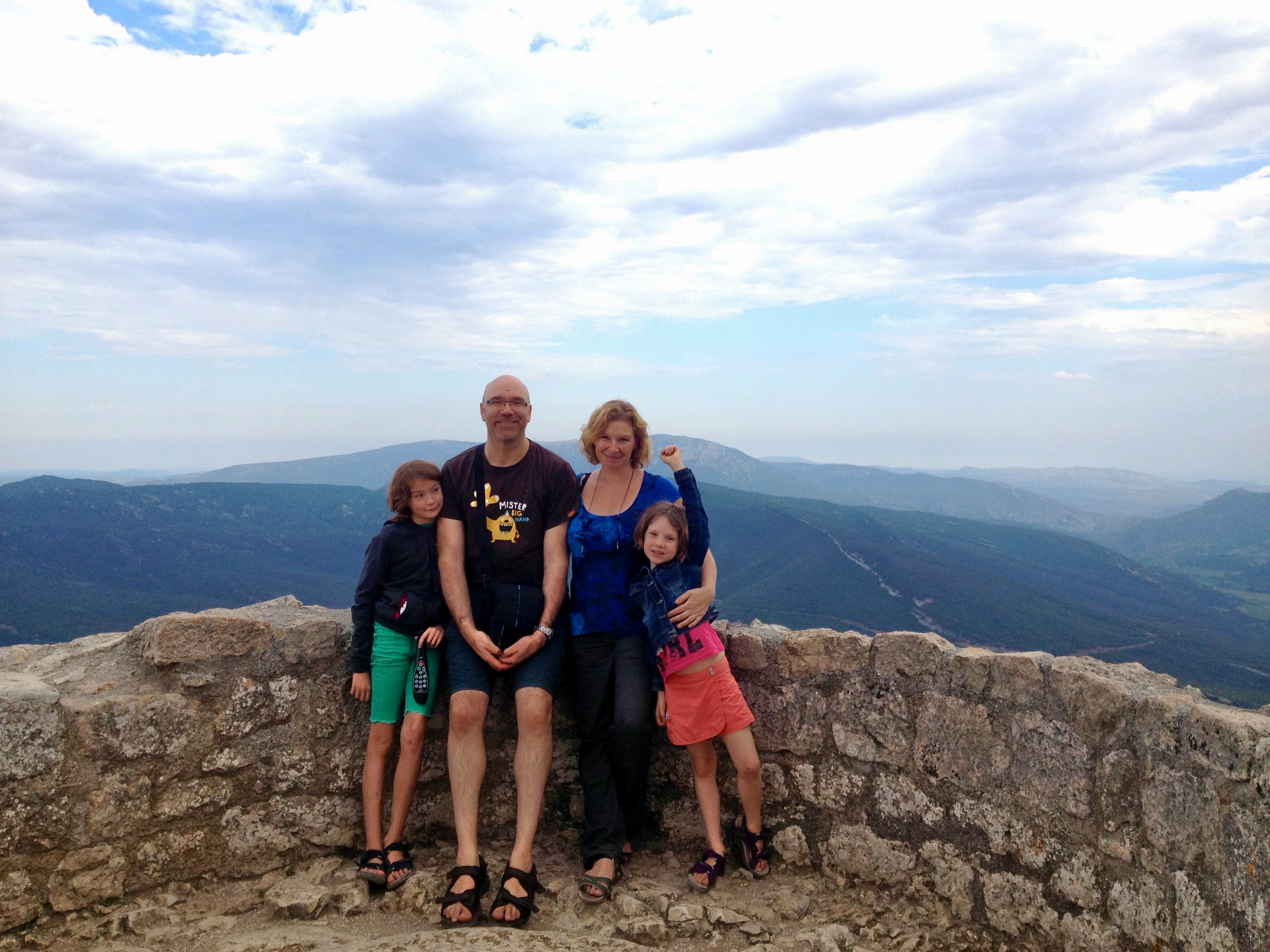 A family stand together at a viewpoint over looking the mountains.