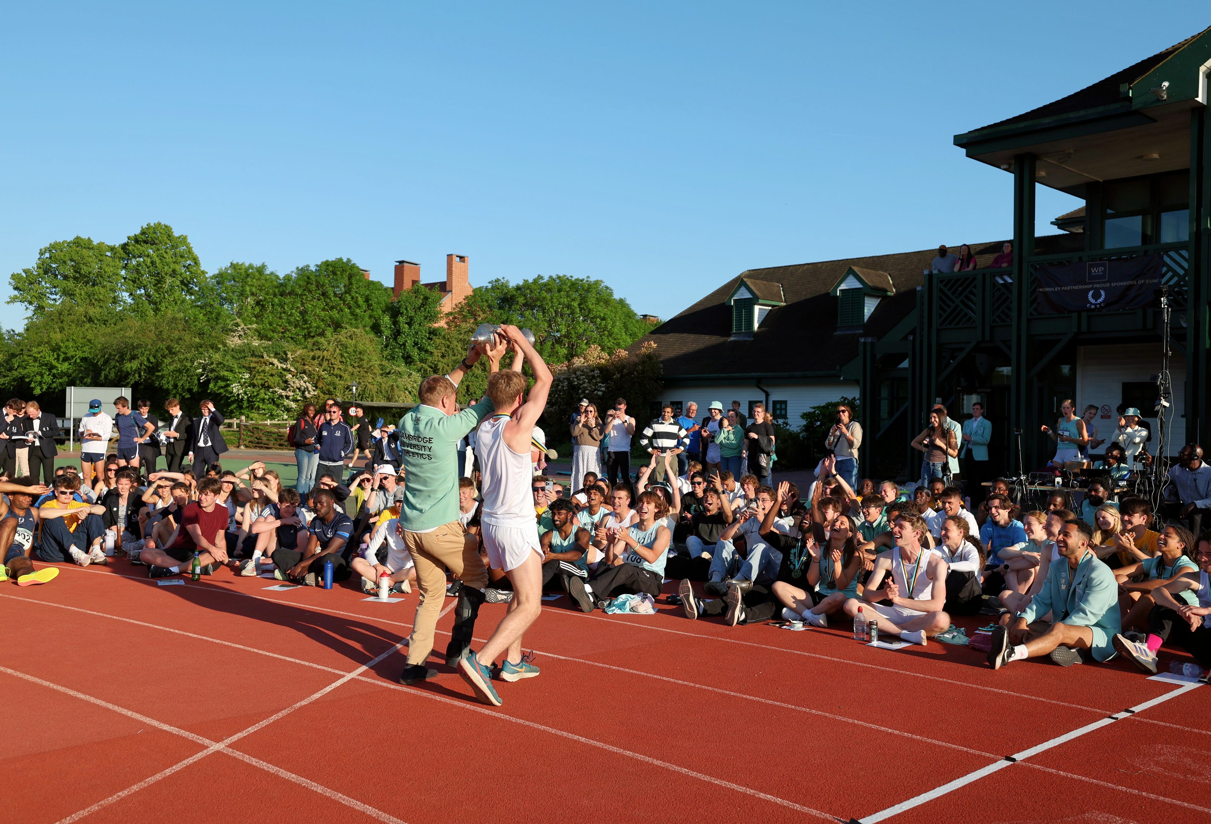 Two male athletes face a crowd of spectators, holding a silver trophy above their heads.
