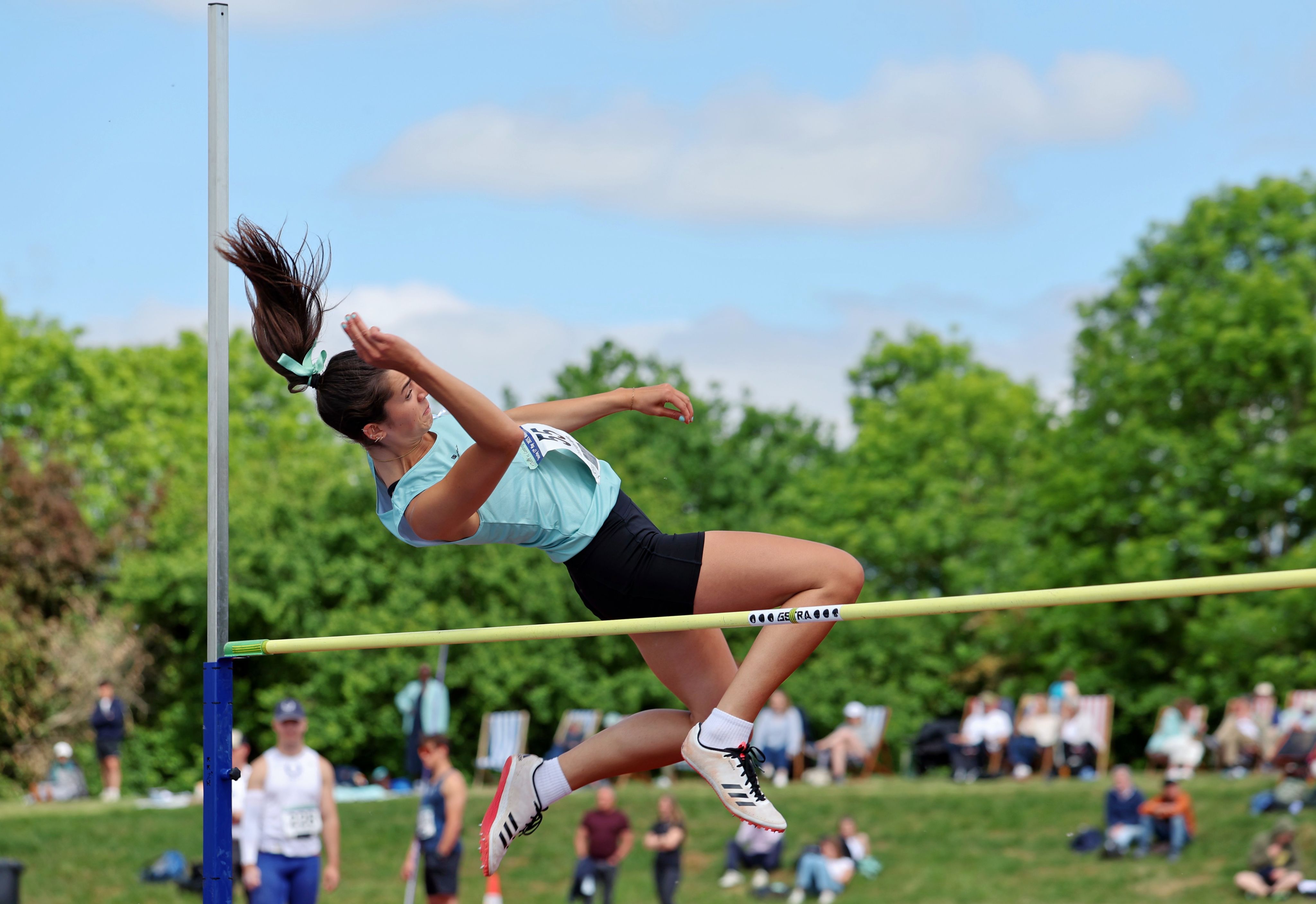 A female athlete leaps backwards over a high jump pole.