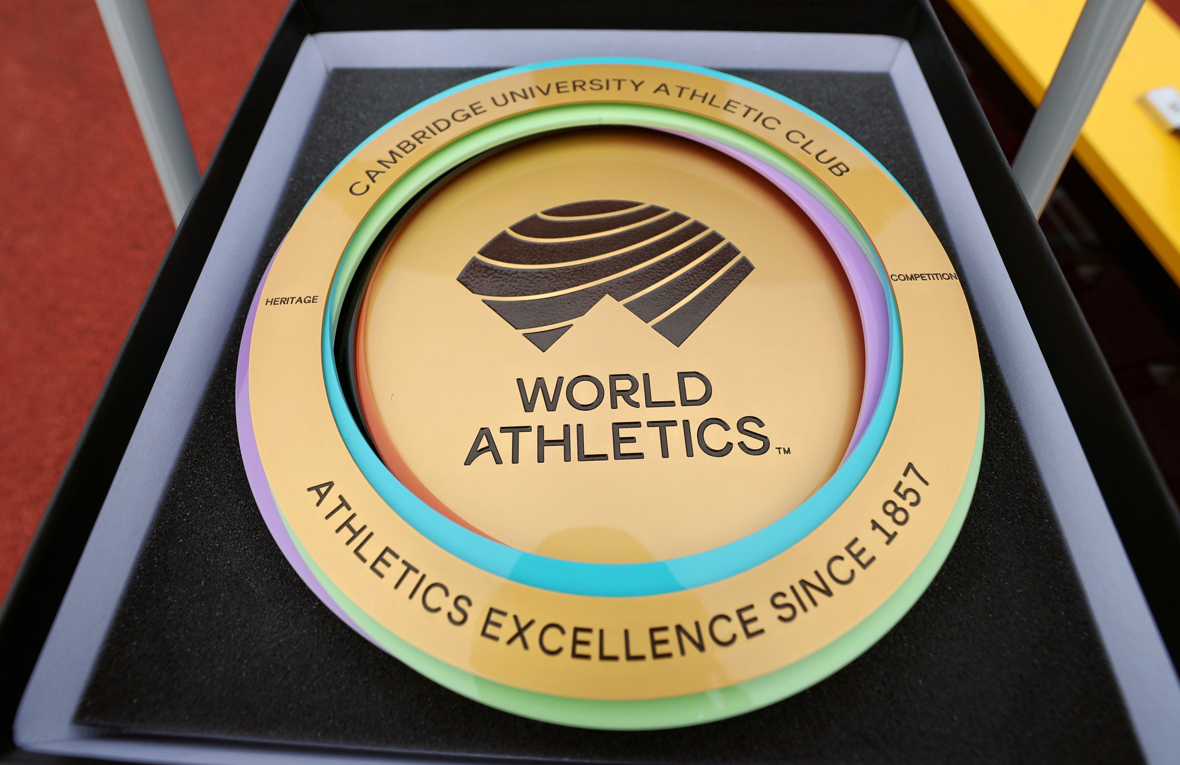 A disc-shaped golden plaque reads: 'Word Athletics. Cambridge University Athletic Club, Athletics Excellence Since 1857.'