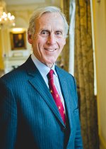 Stuart Laing profile picture standing in a navy pin-stripe suit with a red tie