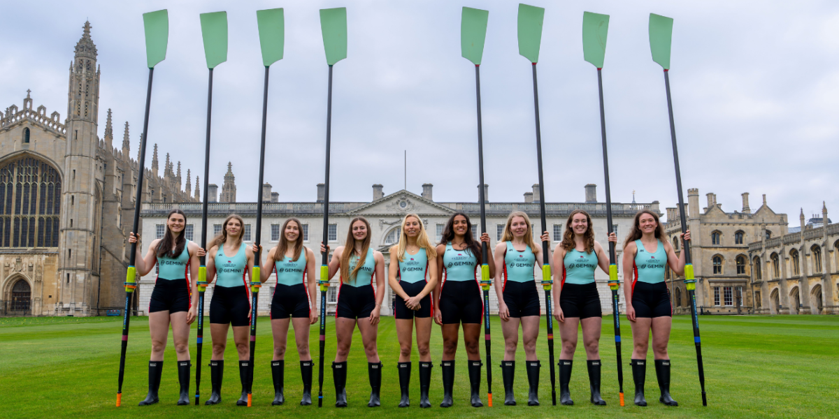 The Cambridge Women's Crew stand in a single line, holding their blades vertically towards the sky.