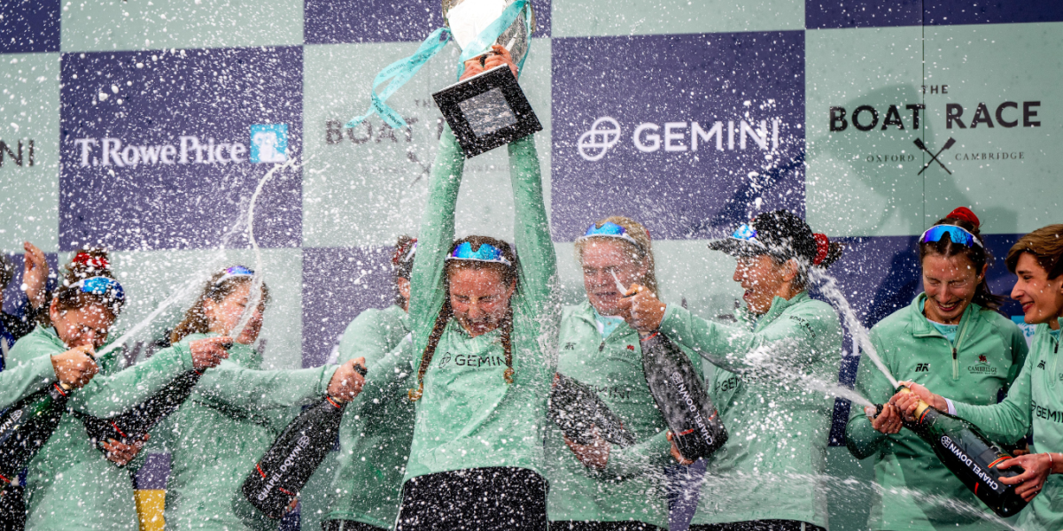 The 2023 women's crew celebrate victory, holding the trophy high and spraying champagne.