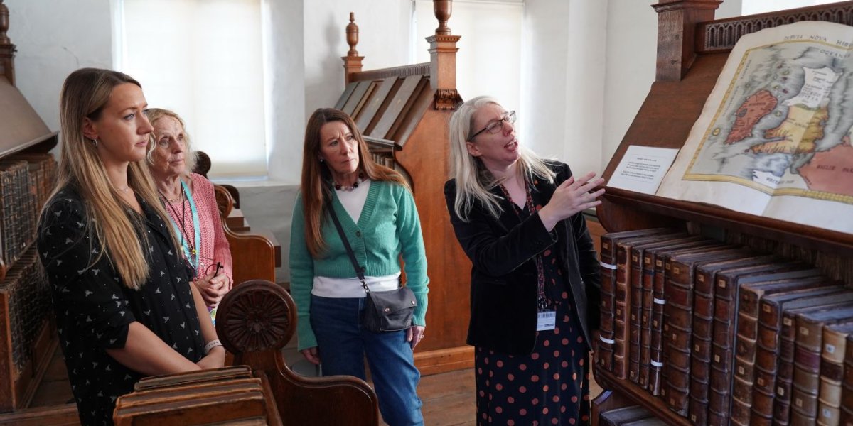 Visitors stand around a decorated manuscript in an oak library.