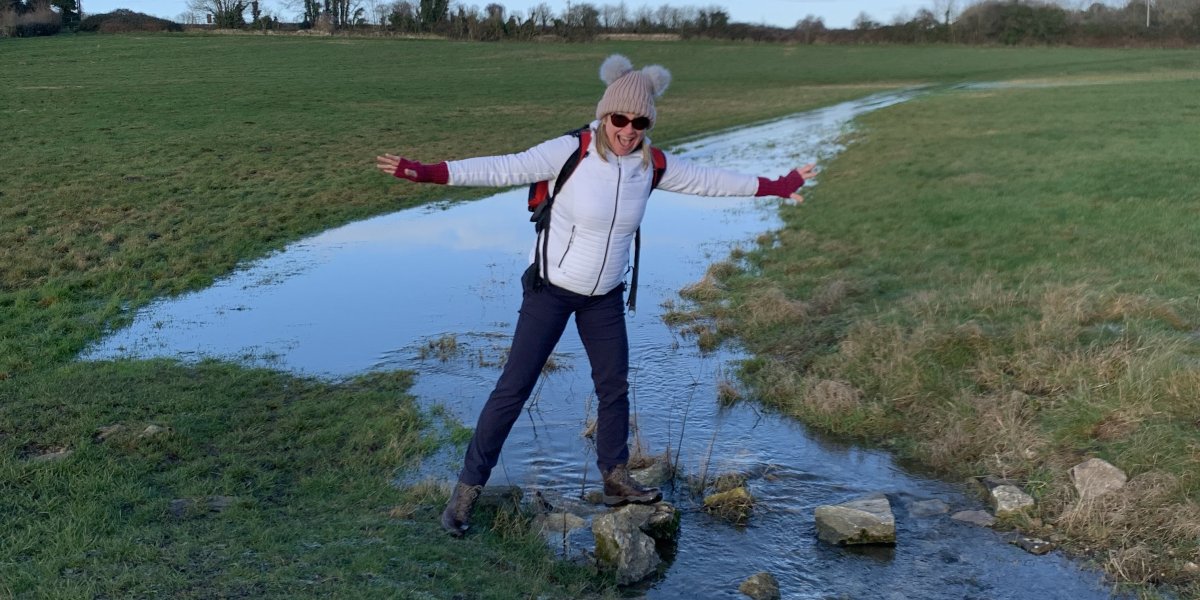 Claire stands in outdoor gear on a stepping stone at the source of Thames.