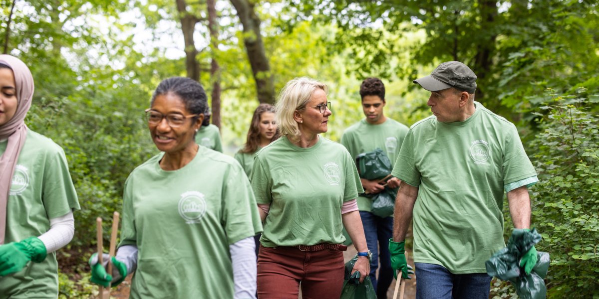 Getty image library photograph showing a group of volunteers walking through a wooded location in green tops and carrying tools