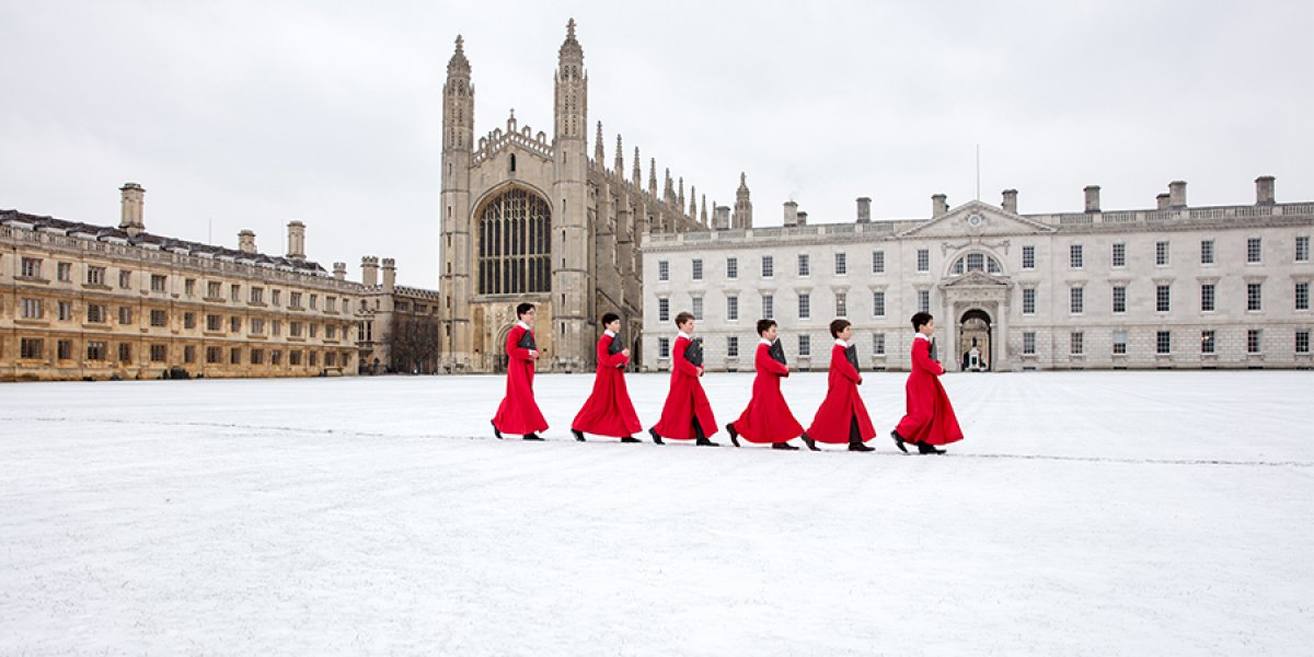 Choirboys from King's College Choir walking in the snow in front of the chapel