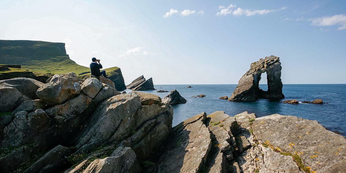 Man sitting on the coastal rocks looking out to the Gaada Stack