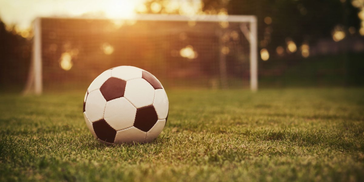 A football sits on a grass pitch while the sun sets.