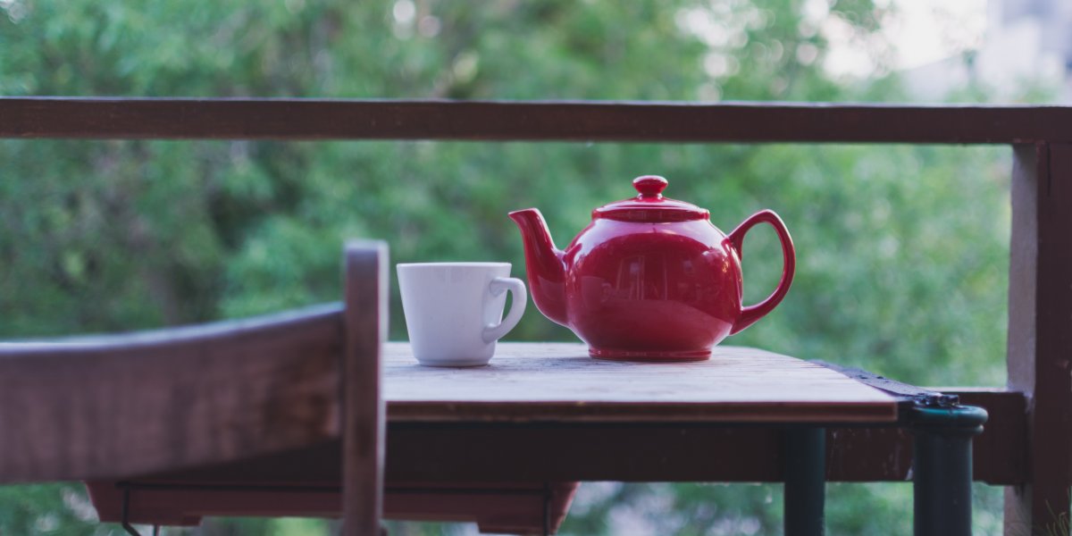 Red teapot on a table with green scenery in the background