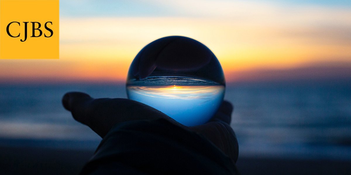 Hand with a clear sphere showing the sunset with CJBS logo in top left corner