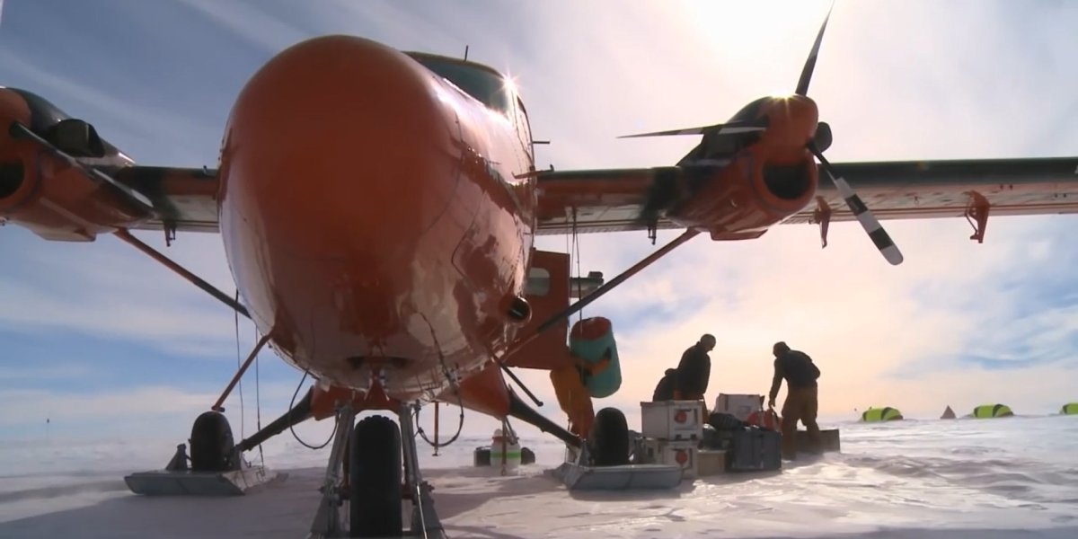 A plane sits in a snowy landscape while researchers unload cargo