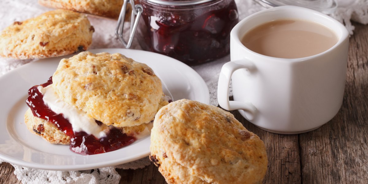 Scones filled with jam and cream sit on a plate alongside a cup of tea and a jar of jam.
