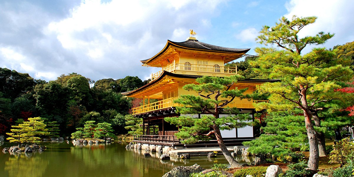 Three storey Japanese building in yellow overlooking the river with cloudy skies above